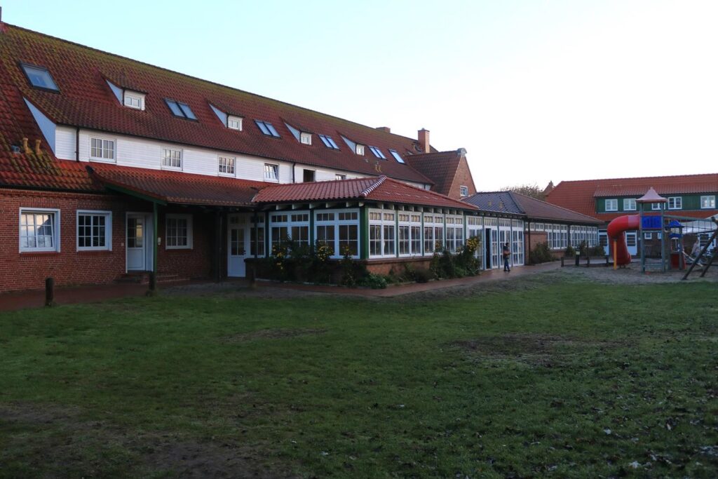 Die Ansicht eines Schulgebäudes mit Spielplatz und Rasenfläche.