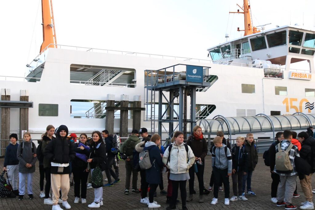 Gruppe von Schülern wartet an einem Fähranleger neben einem Schiff.