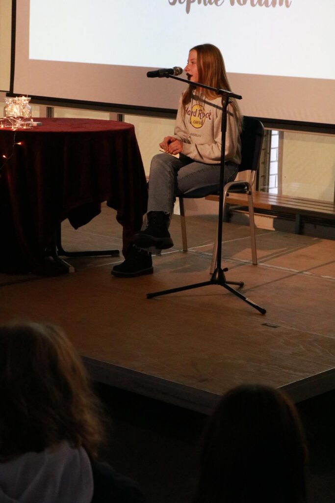 Schülerin sitzt an einem Tisch mit Mikrofon während einer Veranstaltung.