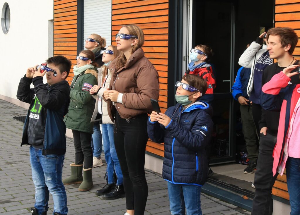 Schüler und Erwachsene beobachten mit speziellen Brillen einen Himmel.