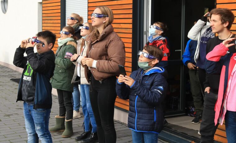Schüler und Erwachsene beobachten mit speziellen Brillen einen Himmel.