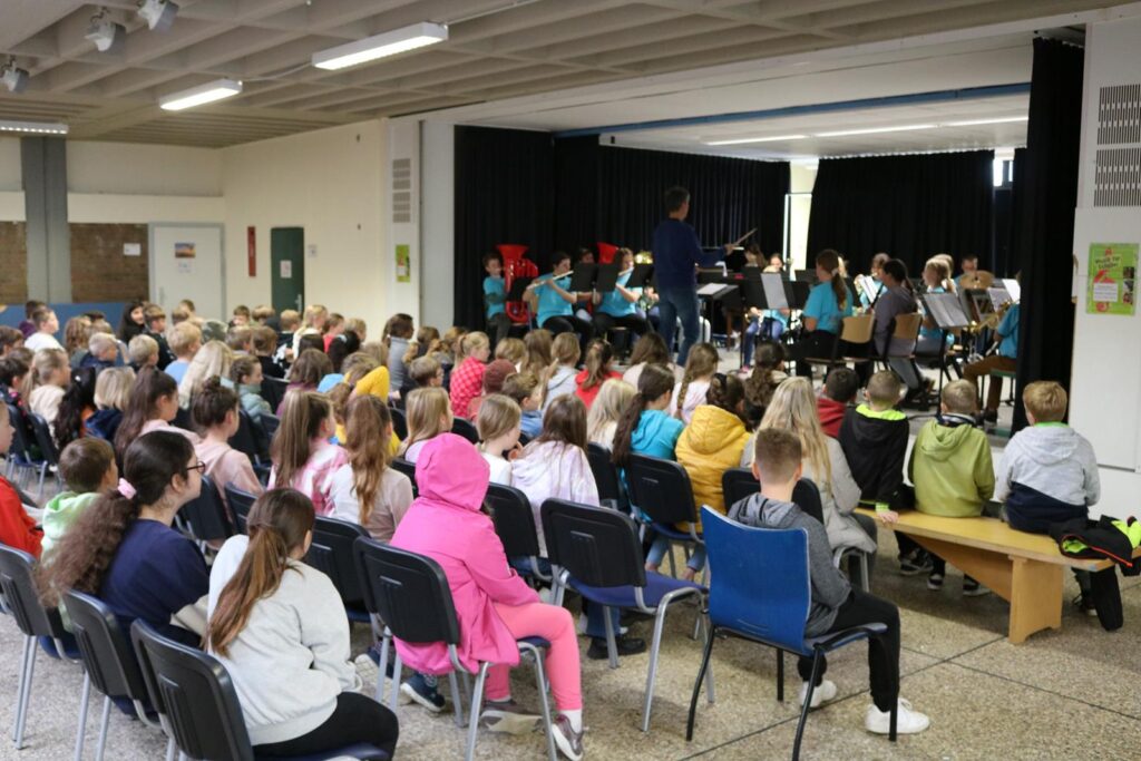Schüler sitzen auf Stühlen und verfolgen ein Konzert auf der Bühne.