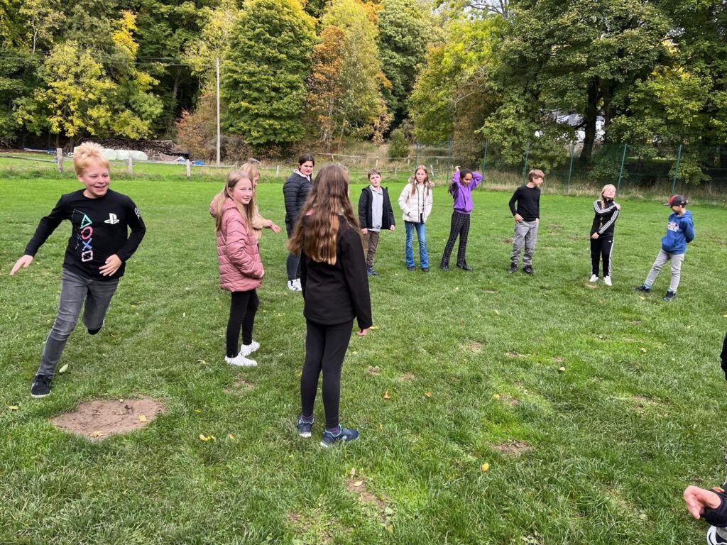Schüler spielen auf einer Wiese, einige lachen und bewegen sich aktiv.