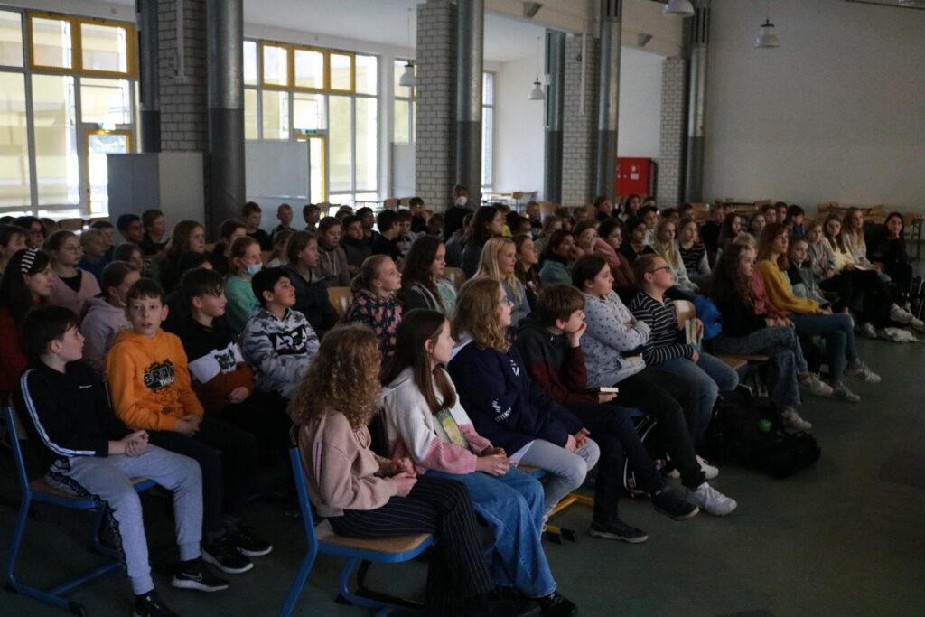 Schüler sitzen in einem Saal und hören aufmerksam zu.