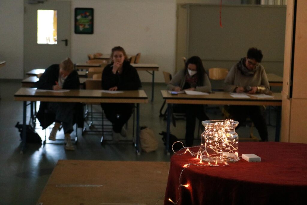 Schülerinnen und Schüler sitzen an Tischen und schreiben. Im Vordergrund leuchtet ein Dekoobjekt.