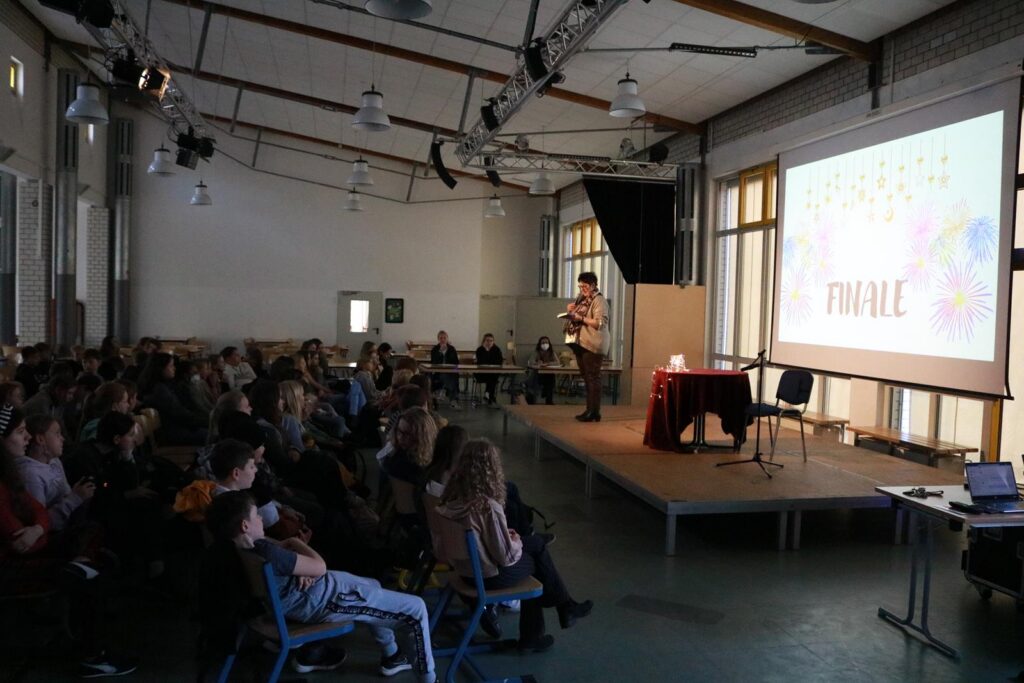 Veranstaltung in einem großen Raum mit Publikum und Bildschirmpräsentation.