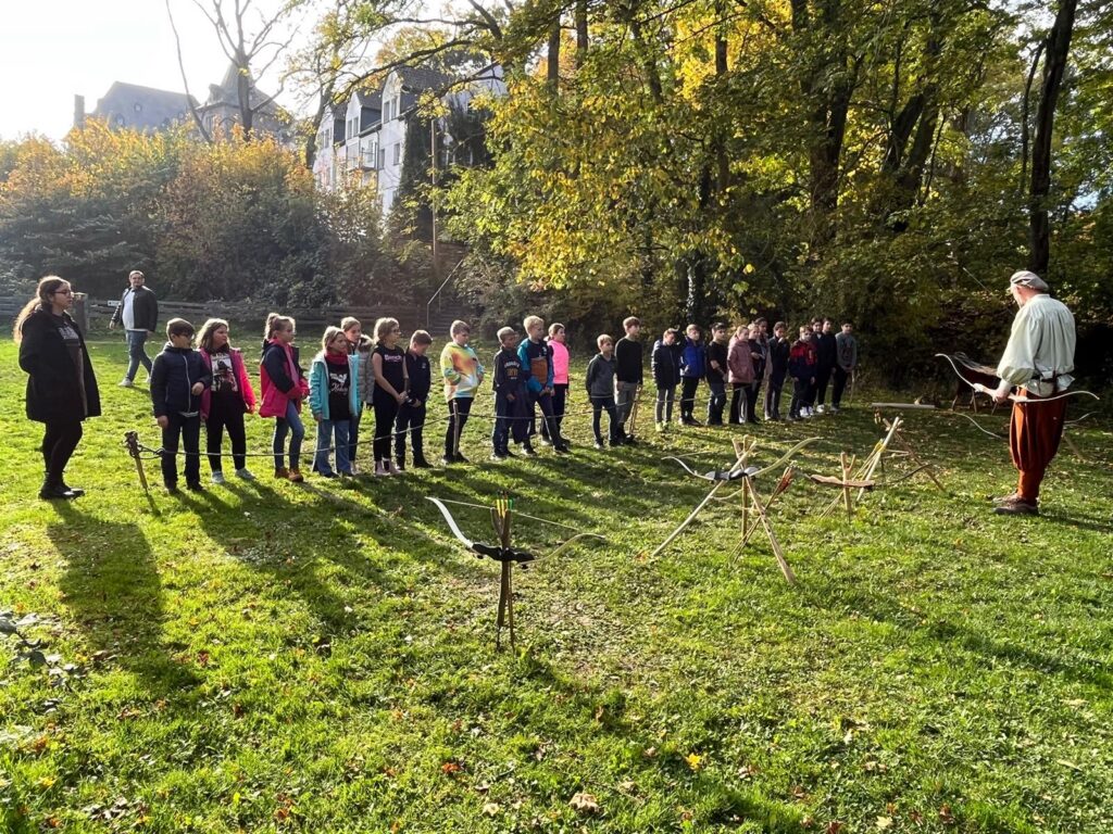 Gruppe von Schülern im Freien, beobachtet eine Person, die etwas demonstriert.