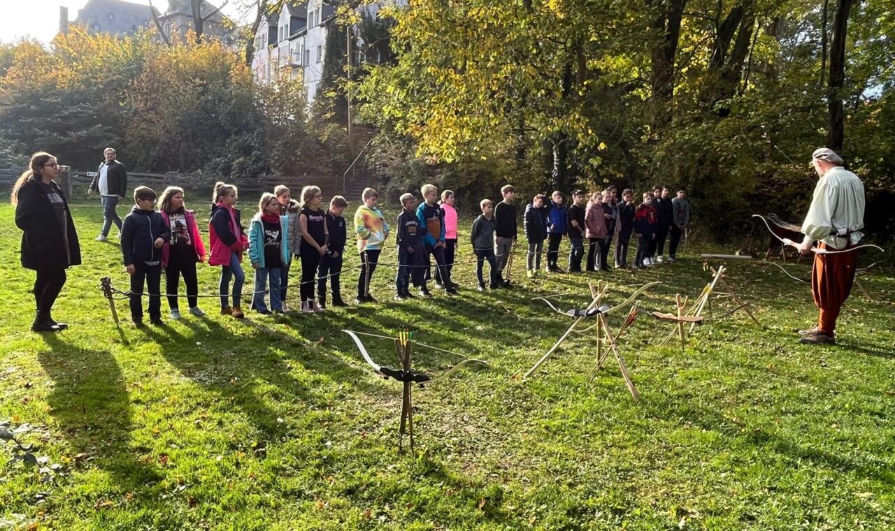 Gruppe von Schülern im Freien, beobachtet eine Person, die etwas demonstriert.