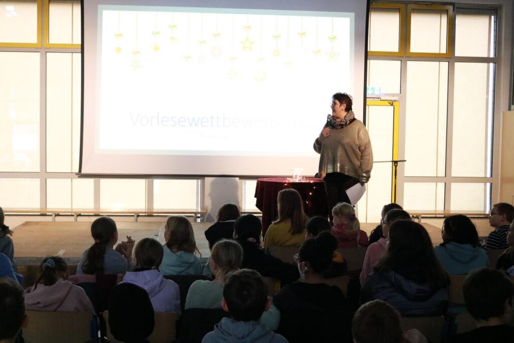Ein Lehrer spricht vor einer Gruppe von Schülern in einem Klassenraum.