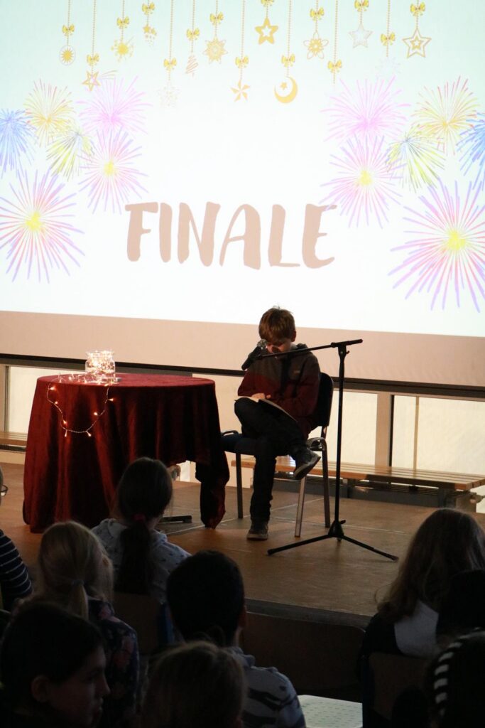 Kind sitzt auf der Bühne und liest beim Finale vor einem Publikum.