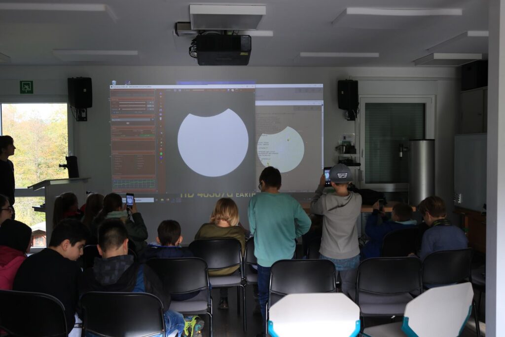Schüler sitzen in einem Klassenraum und schauen auf ein Projektorbild.