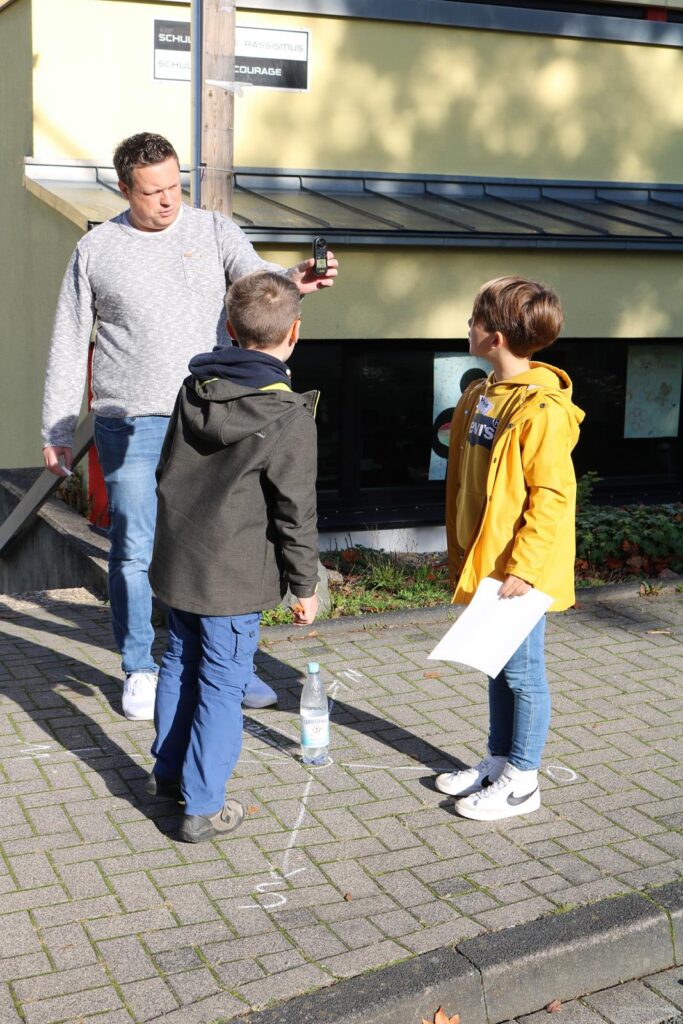 Ein Erwachsener spricht mit zwei Kindern auf einem Gehweg.