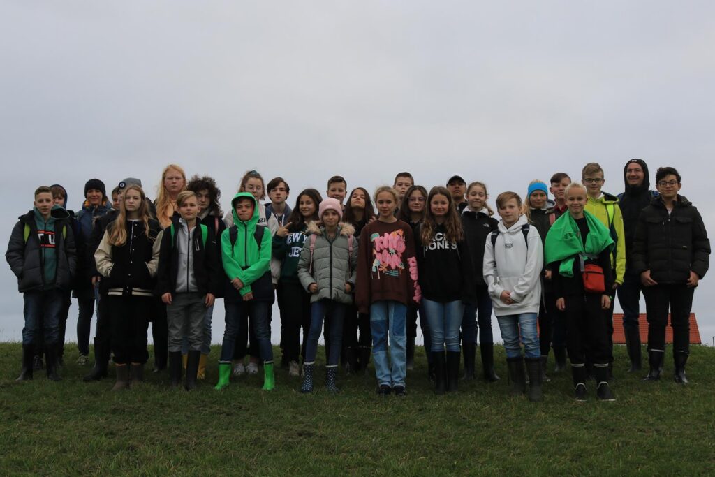 Gruppe von Schülern und Lehrern steht auf einer Wiese, grauer Himmel im Hintergrund.