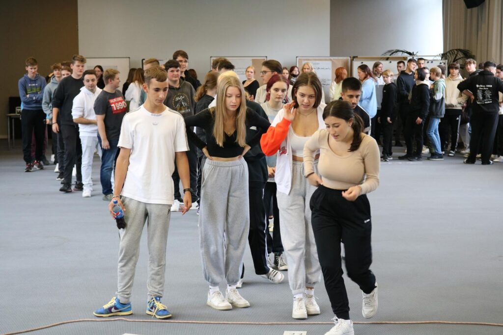 Schülerinnen und Schüler gehen gemeinsam über einen markierten Bereich in einem großen Raum.