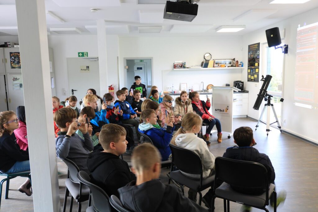 Schüler sitzen in einem Klassenzimmer und schauen einen Bildschirm.