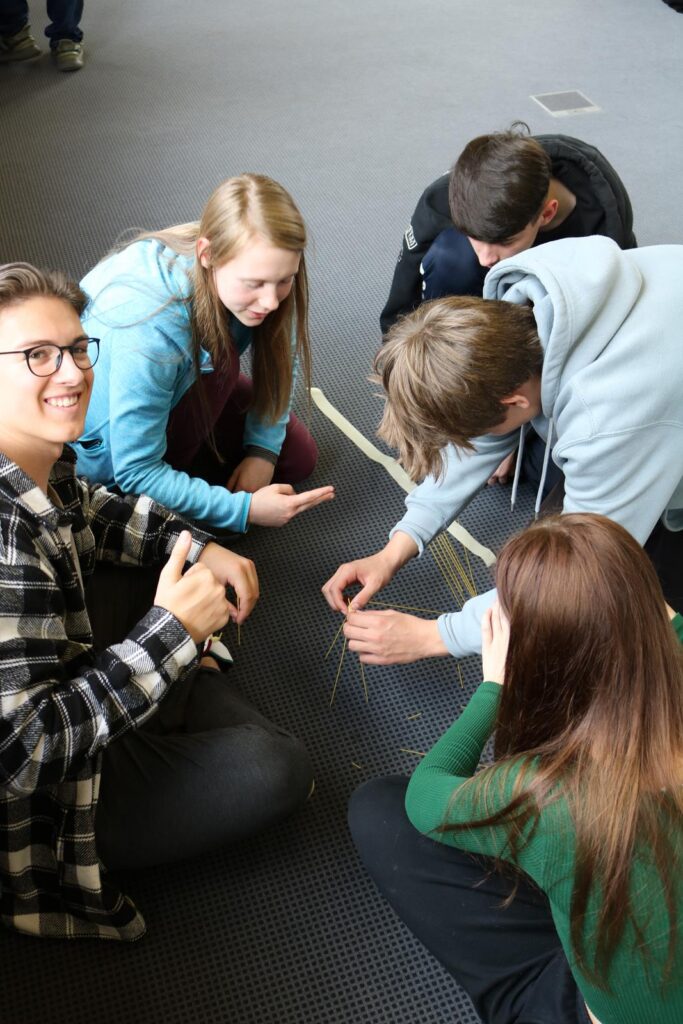 Schülerinnen und Schüler sitzen auf dem Boden und arbeiten gemeinsam an einem Projekt.