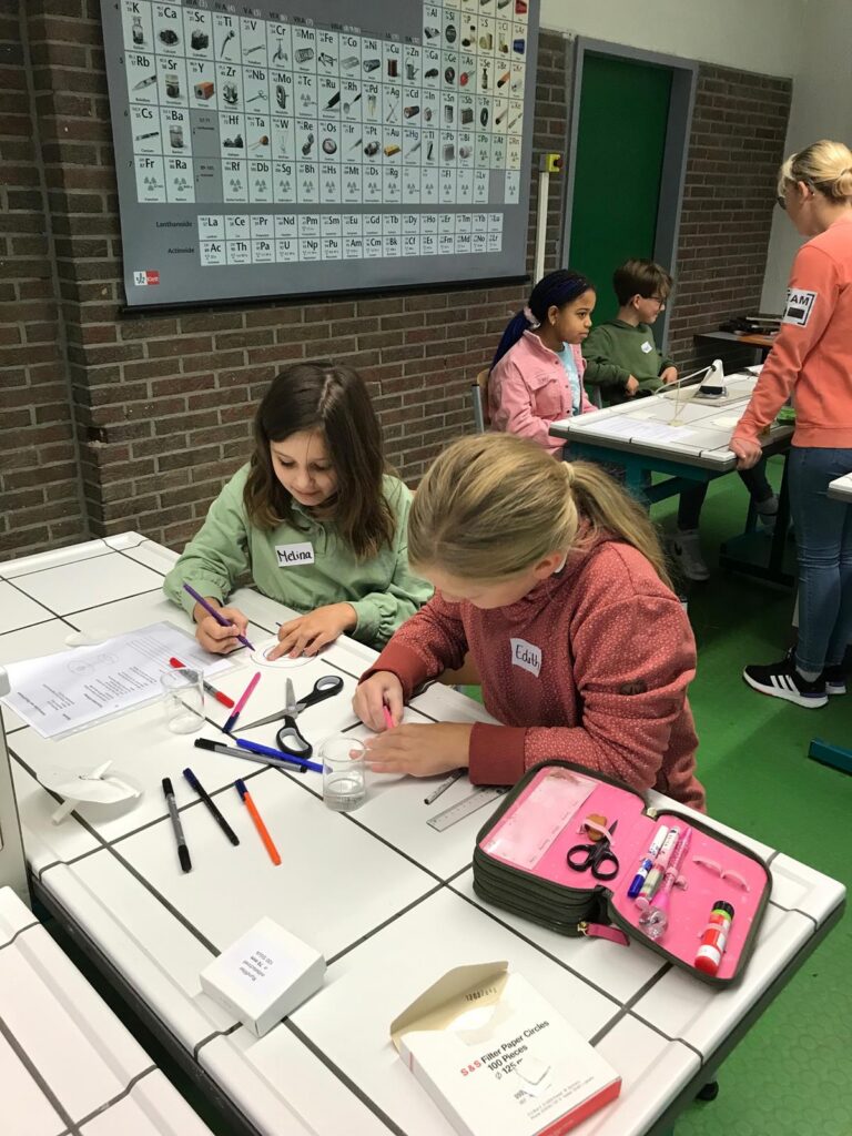 Schülerinnen basteln an Tisch mit Stiften, Scheren und Papier.