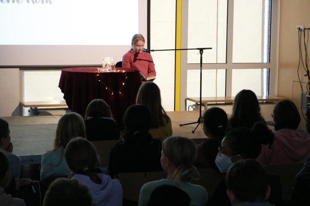 Lesung mit einem Vortragenden an einem Tisch, Schüler sitzen im Publikum.
