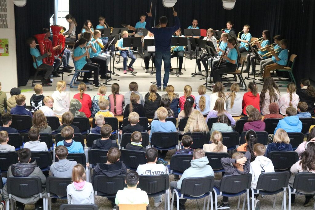 Schulorchester spielt vor Publikum in einer Aula.