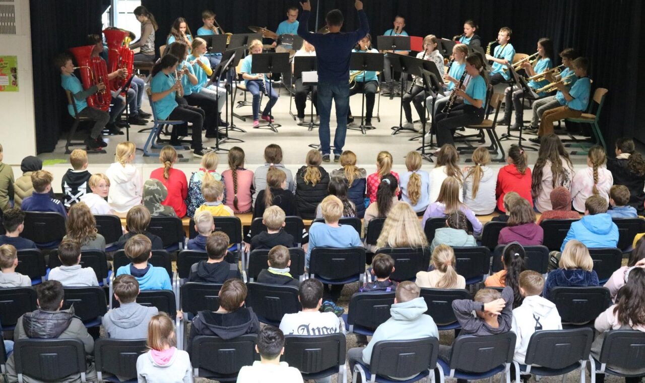 Schulorchester spielt vor Publikum in einer Aula.
