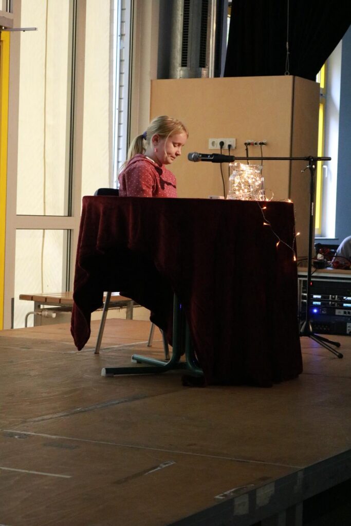 Frau sitzt an einem Tisch mit Mikrofon auf einer Bühne.