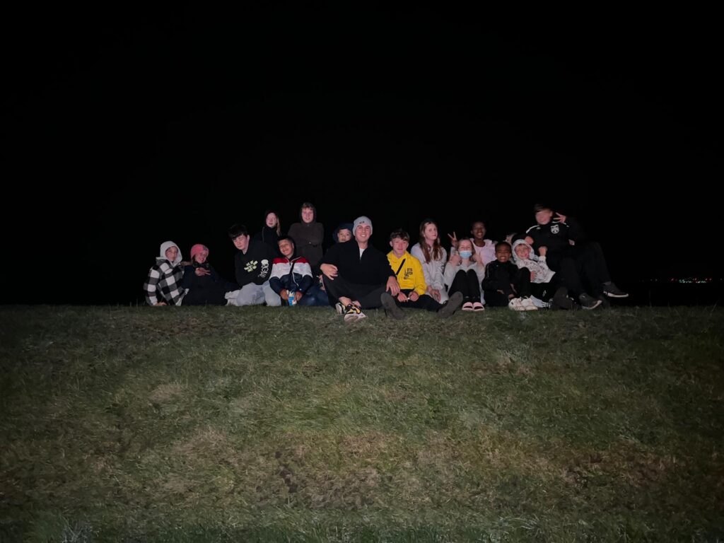 Gruppe von Jugendlichen sitzt auf einer Wiese bei Nacht.