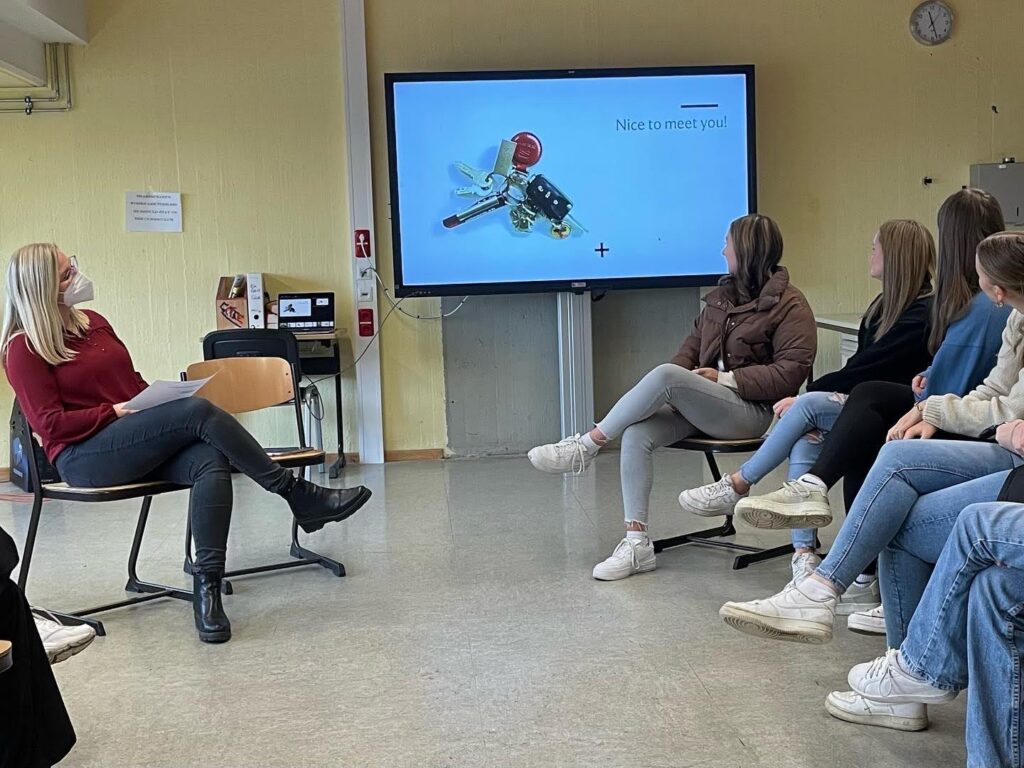 Schülerin präsentiert vor Klasse, Projektion eines technischen Geräts im Hintergrund.