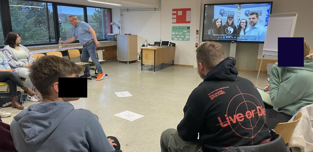Gruppensitzung in einem Klassenraum mit Teilnehmern und Präsentation an der Wand.