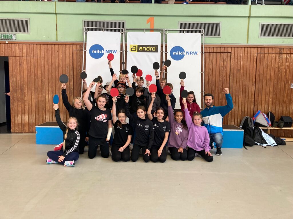 Gruppenshooting von Kindern mit Tischtennis-Schlägern in einer Sporthalle.