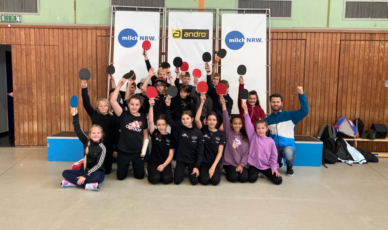 Gruppenshooting von Kindern mit Tischtennis-Schlägern in einer Sporthalle.
