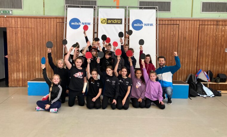 Gruppenshooting von Kindern mit Tischtennis-Schlägern in einer Sporthalle.