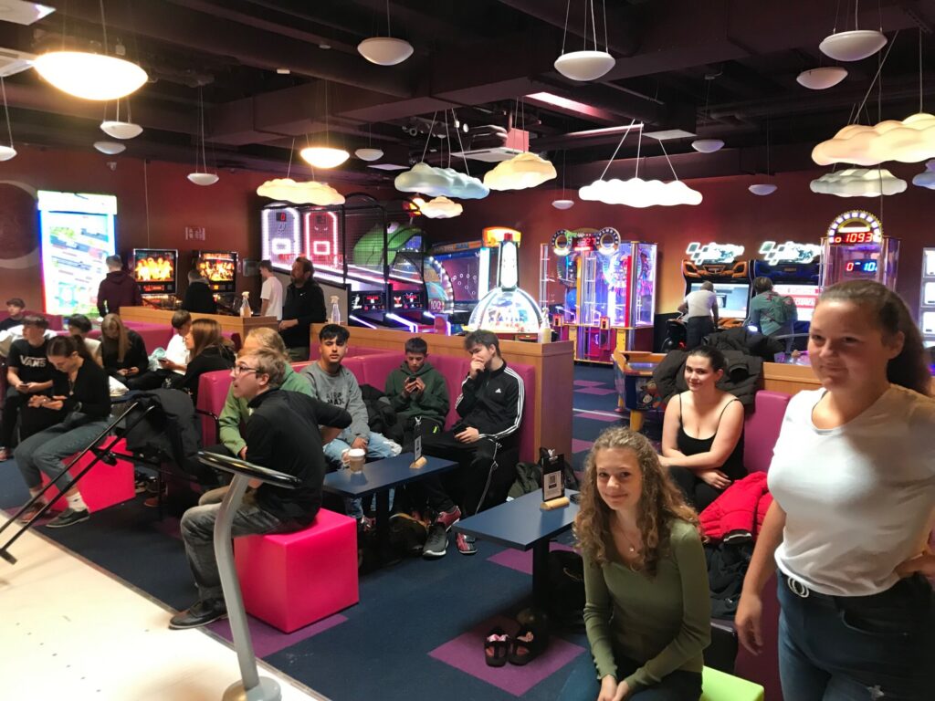 Gruppe von Jugendlichen in einer Spielhalle mit Arcade-Spielen und bunten Sitzgelegenheiten.