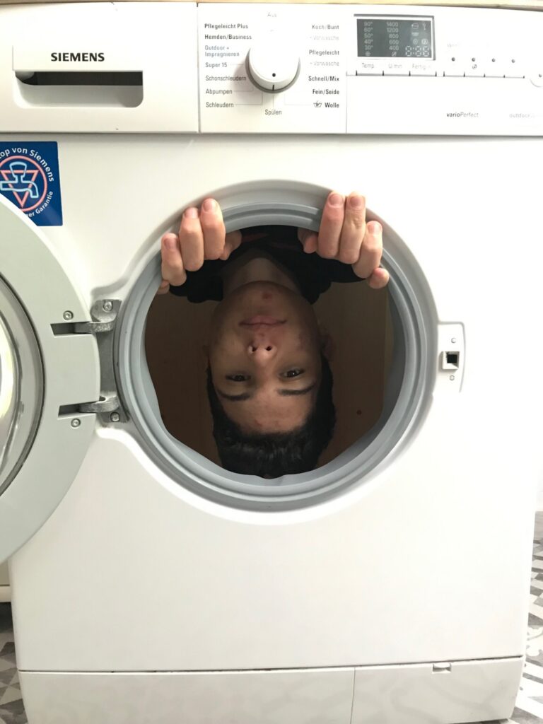 Junge schaut aus der Tür einer Waschmaschine.