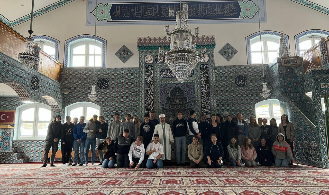 Gruppenfoto von Menschen in einem Moscheeraum mit dekorativen Elementen.
