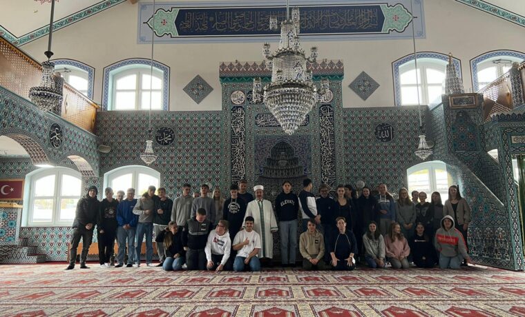 Gruppenfoto von Menschen in einem Moscheeraum mit dekorativen Elementen.