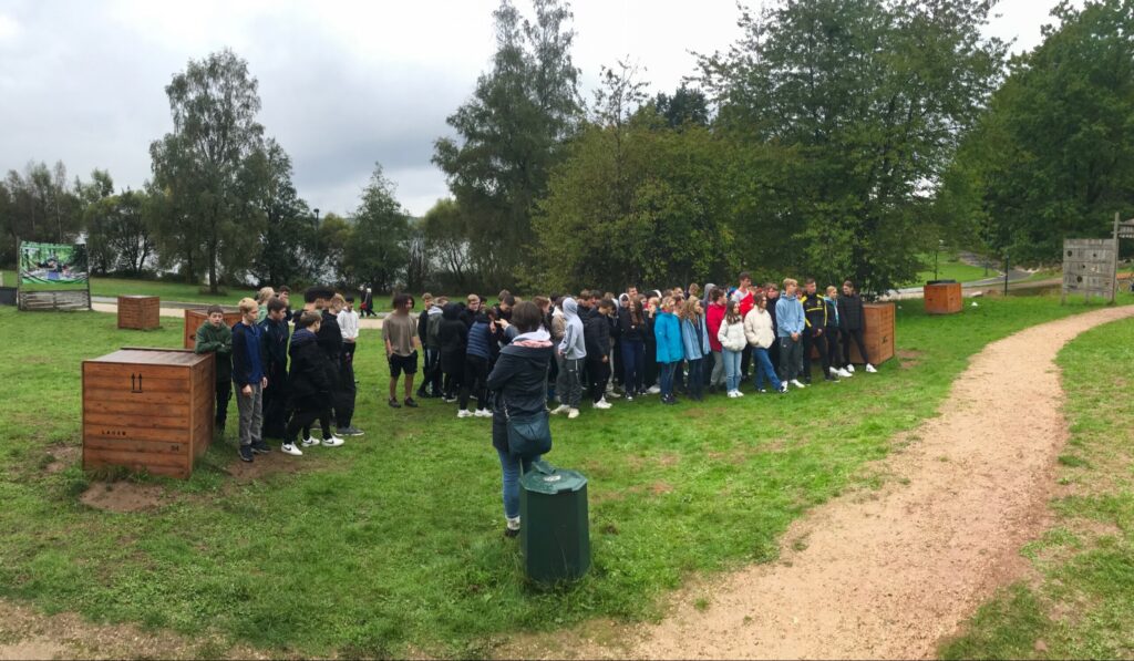 Schülergruppe versammelt sich im Freien auf einem grünen Gelände.