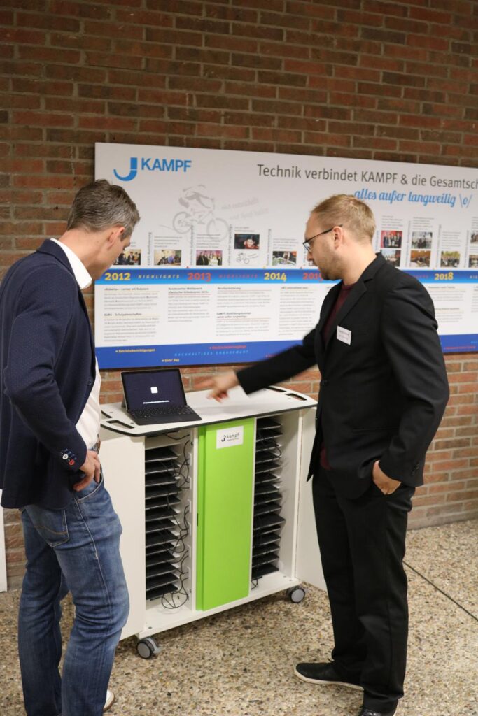 Zwei Männer betrachten einen Laptop neben einem mobilen Präsentationswagen.