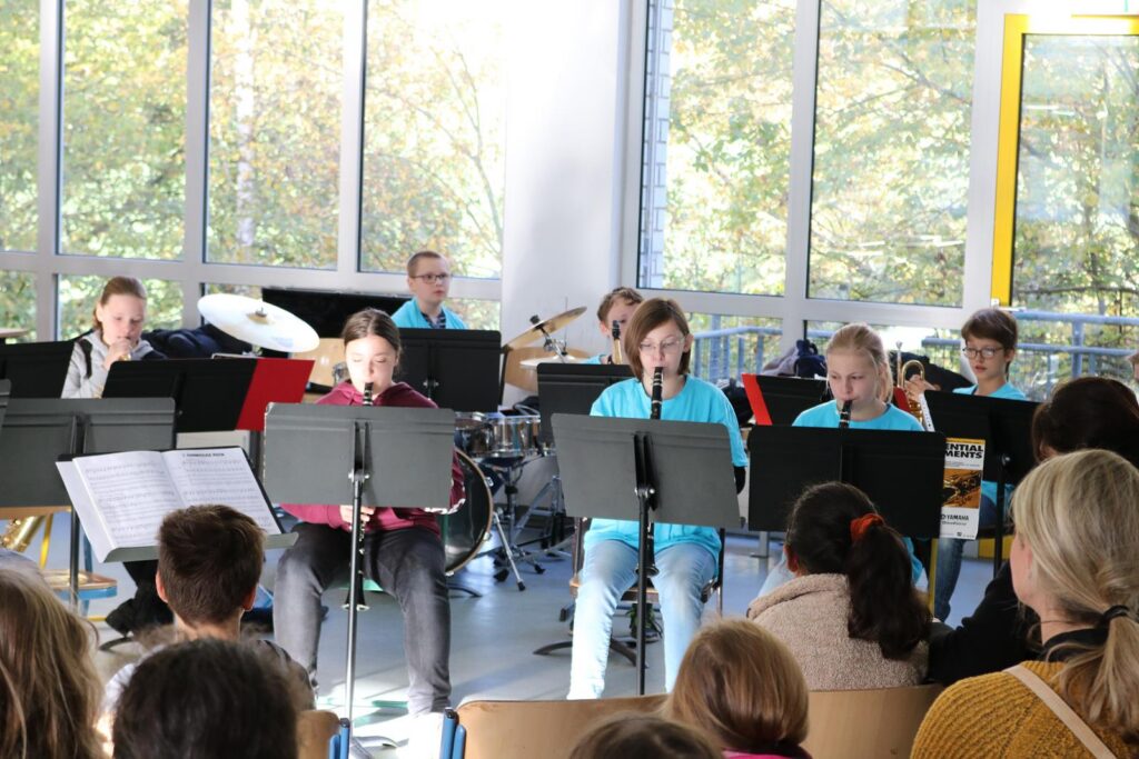 Schüler musizieren in einer Aula, Publikum sitzt im Vordergrund.