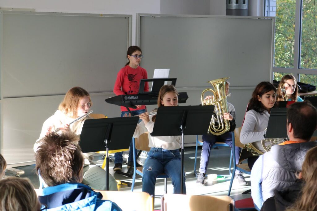 Schüler spielen in der Aula ein Musikstück vor Publikum.