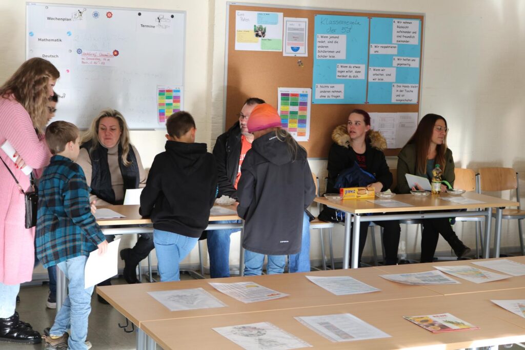 Eltern und Schüler stehen an Tischen in einem Klassenraum.