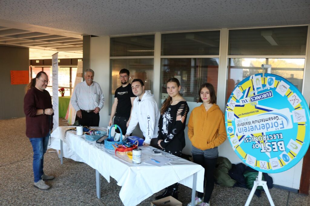 Gruppe von Personen an einem Tisch mit Informationsmaterial und einem Glücksrad.