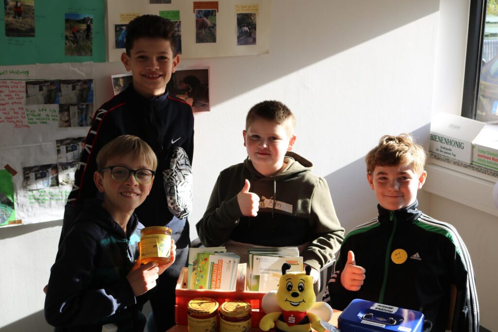 Vier Schüler zeigen Daumen hoch vor einem Tisch mit verschiedenen Gegenständen.