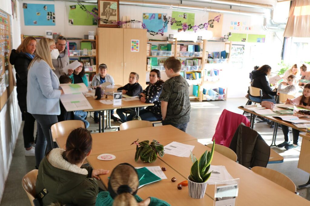 Schüler und Lehrer in einem Klassenraum, Tische mit Unterrichtsmaterialien.