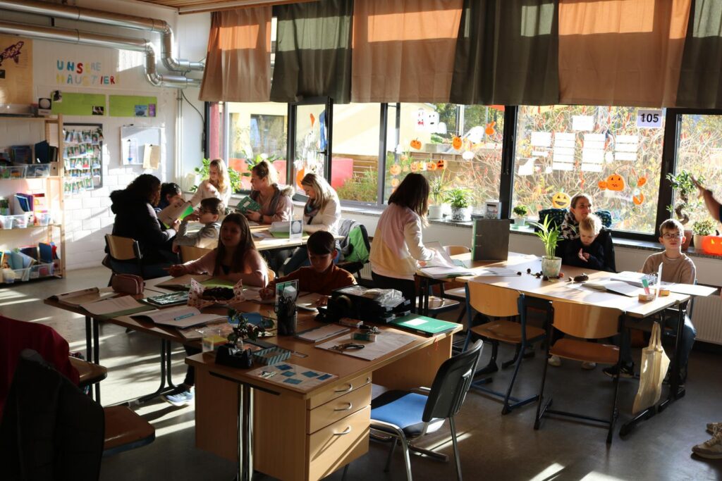 Schulkontakt: Schüler und Lehrer in einem Klassenzimmer mit großen Fenstern.