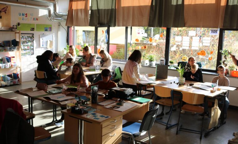 Schulkontakt: Schüler und Lehrer in einem Klassenzimmer mit großen Fenstern.