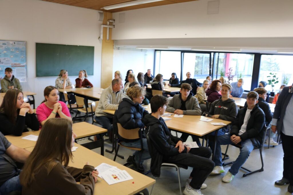 Schüler und Lehrer sitzen in einem Klassenraum und diskutieren.