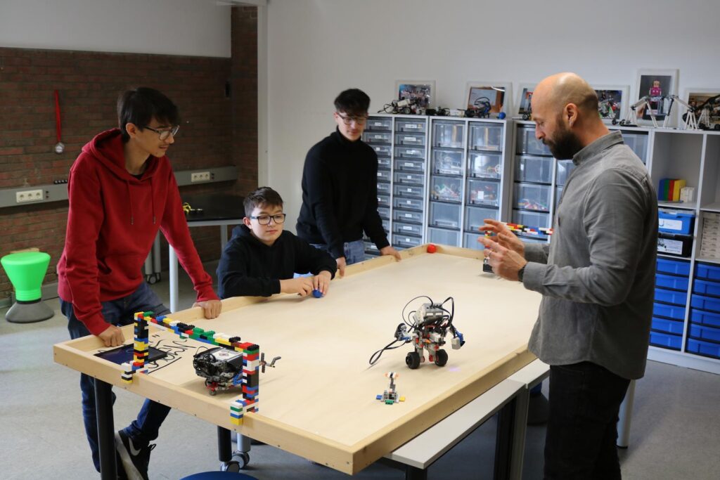 Schüler und Lehrer arbeiten an einem Tisch mit Robotikmaterialien.