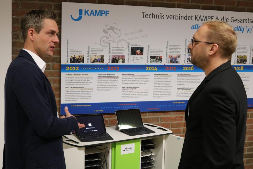 Zwei Männer unterhalten sich vor einer Zeitlinie und Laptops.