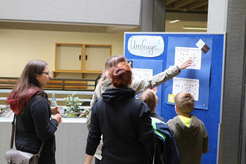 Personen betrachten eine Umfrage an einem Pinnwand-Board in einem Schulgebäude.