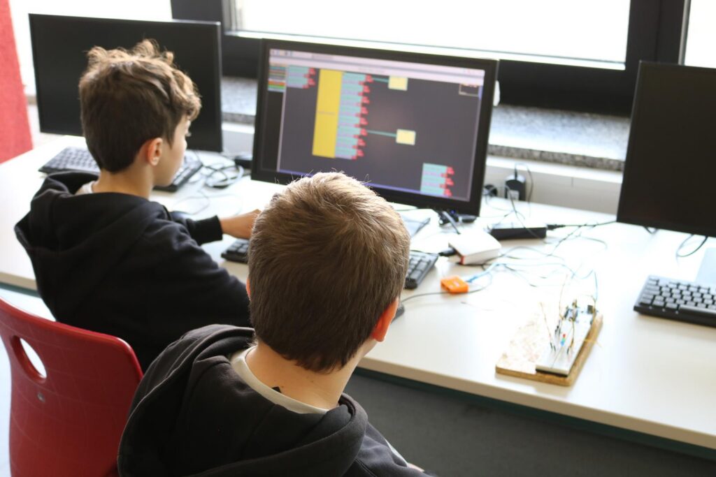Zwei Schüler sitzen an Computern und arbeiten an einem Projekt.